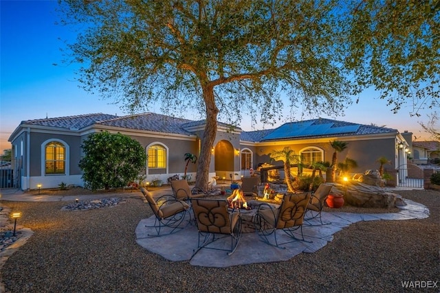 back of property with a patio, an outdoor fire pit, solar panels, and stucco siding