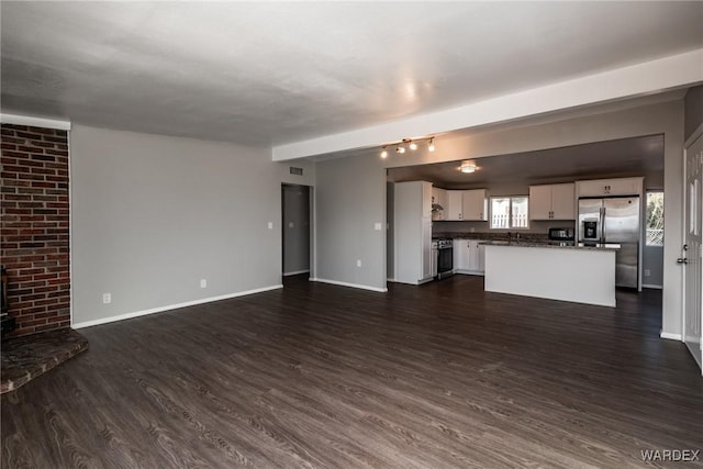 unfurnished living room featuring a wood stove, baseboards, and dark wood-style flooring