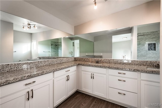 bathroom featuring double vanity, wood finished floors, a stall shower, and a sink