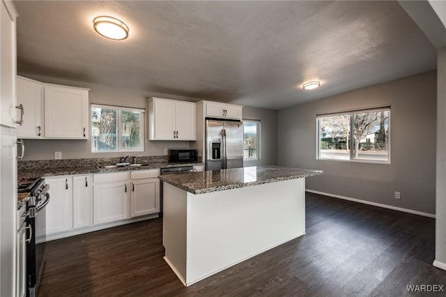 kitchen with appliances with stainless steel finishes, dark stone counters, white cabinetry, and a kitchen island