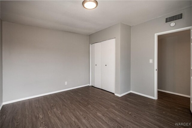 unfurnished bedroom with baseboards, a closet, visible vents, and dark wood-type flooring