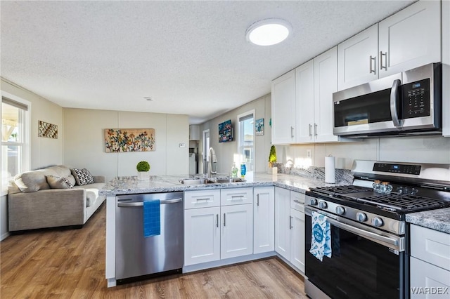 kitchen featuring a peninsula, white cabinetry, appliances with stainless steel finishes, and open floor plan