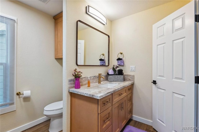 half bath with toilet, vanity, baseboards, and wood finished floors