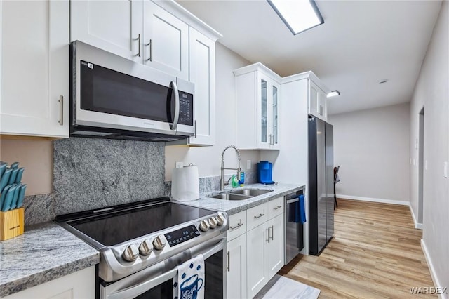 kitchen with glass insert cabinets, appliances with stainless steel finishes, light stone countertops, white cabinetry, and a sink