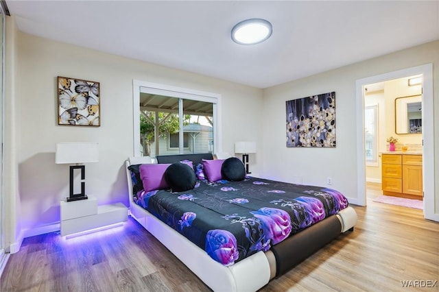 bedroom with connected bathroom, baseboards, and wood finished floors