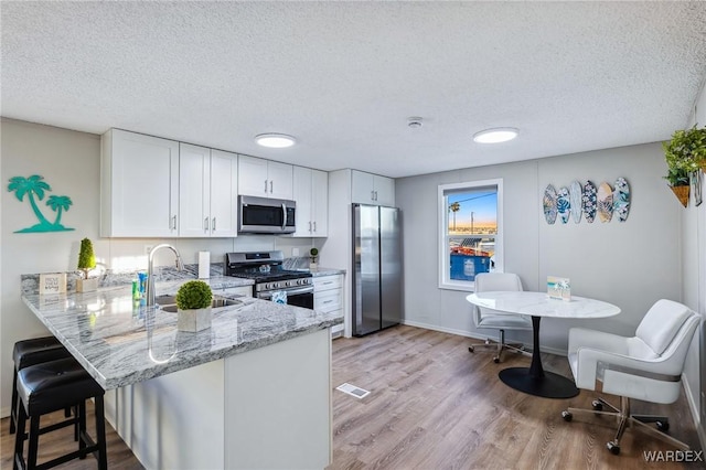 kitchen featuring white cabinets, appliances with stainless steel finishes, a peninsula, light stone countertops, and a sink