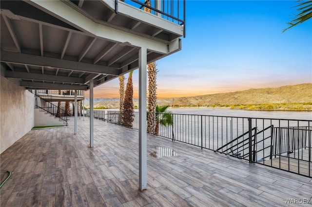 deck at dusk with a patio, stairway, and a water and mountain view