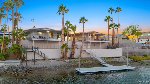 back of property with stairs, a water view, fence, and a balcony