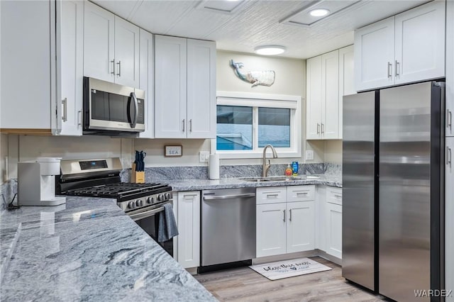 kitchen with appliances with stainless steel finishes, a sink, white cabinetry, and light stone countertops