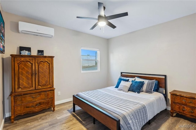 bedroom with ceiling fan, light wood-type flooring, a wall unit AC, and baseboards