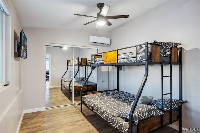 bedroom featuring vaulted ceiling, a wall mounted AC, wood finished floors, and baseboards