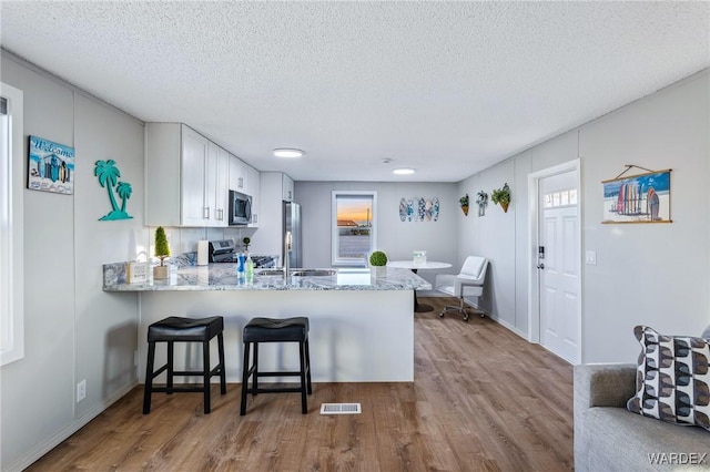 kitchen with a breakfast bar, stainless steel appliances, visible vents, white cabinets, and a peninsula