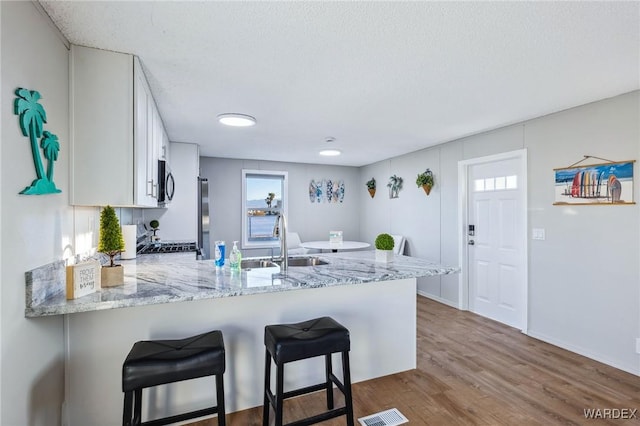 kitchen with white cabinets, a sink, a peninsula, and a breakfast bar area