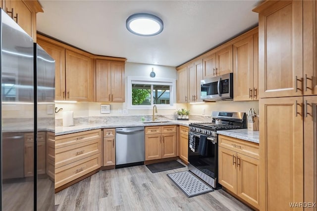 kitchen with stainless steel appliances, light wood-type flooring, a sink, and light stone countertops