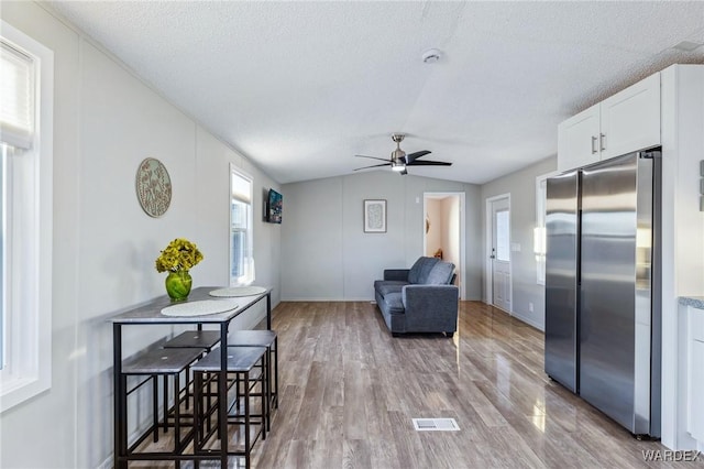 living room with lofted ceiling, a textured ceiling, light wood-type flooring, and visible vents