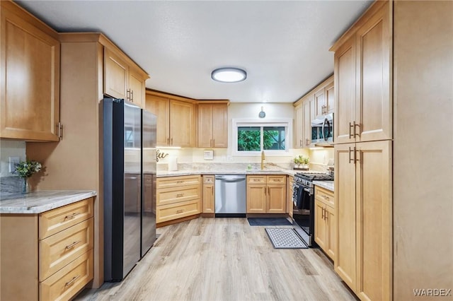 kitchen with light brown cabinets, stainless steel appliances, a sink, light wood-type flooring, and light stone countertops