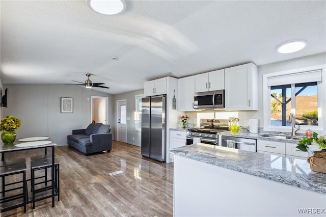 kitchen with stainless steel appliances, light stone counters, a sink, and white cabinetry