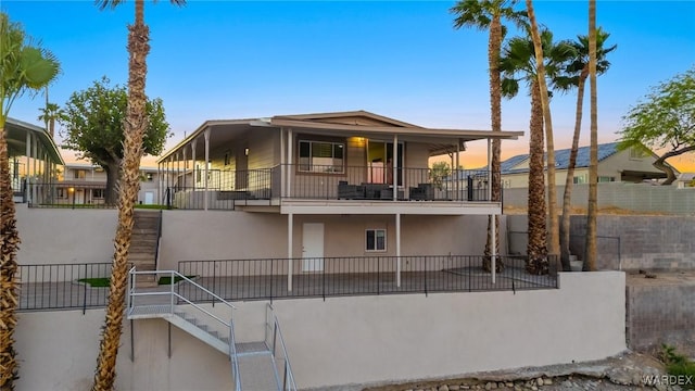 rear view of house featuring a balcony, fence, stairway, and stucco siding