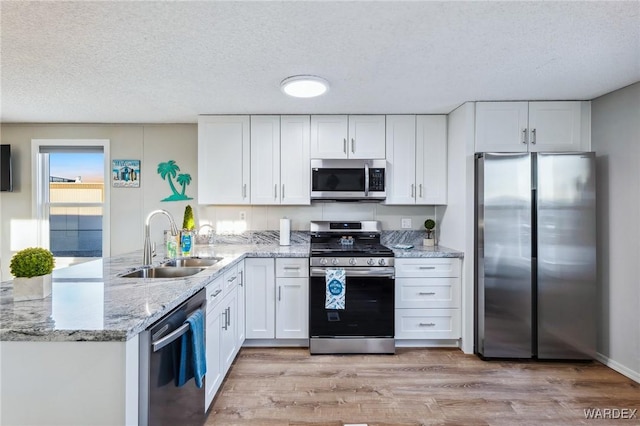 kitchen featuring stainless steel appliances, a peninsula, a sink, white cabinetry, and light stone countertops