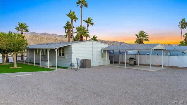 back of property at dusk featuring fence, a mountain view, and central AC