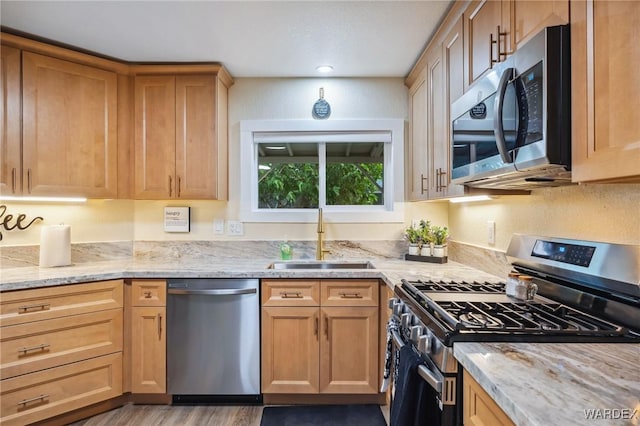 kitchen featuring stainless steel appliances, a sink, light wood finished floors, and light stone counters