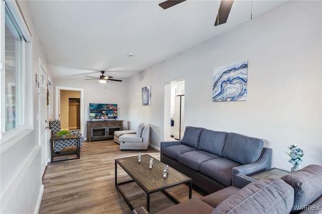 living area featuring ceiling fan, a fireplace, wood finished floors, and baseboards