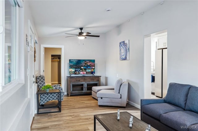 living area with light wood-style floors, ceiling fan, and baseboards