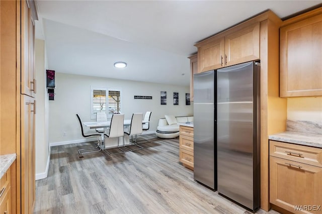 kitchen featuring light wood-style floors, baseboards, light stone counters, and freestanding refrigerator