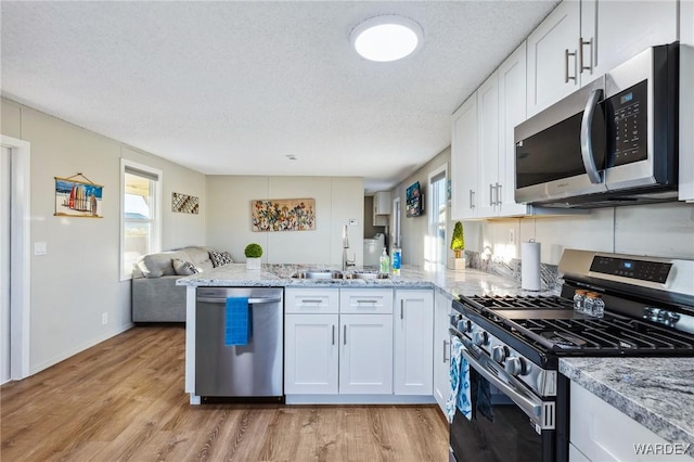 kitchen featuring open floor plan, a peninsula, stainless steel appliances, a healthy amount of sunlight, and white cabinetry