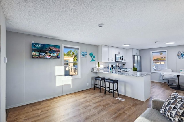 kitchen featuring a peninsula, appliances with stainless steel finishes, light wood-style flooring, and white cabinetry