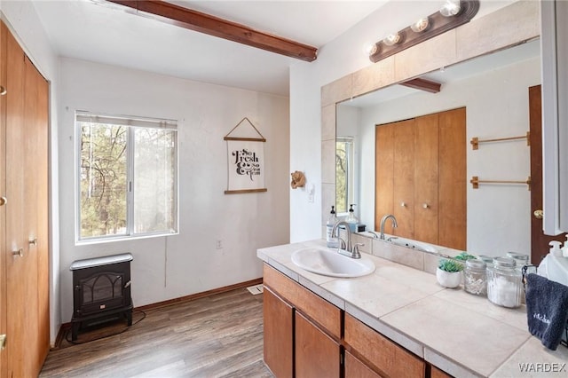 bathroom with vanity, a wood stove, wood finished floors, beam ceiling, and baseboards