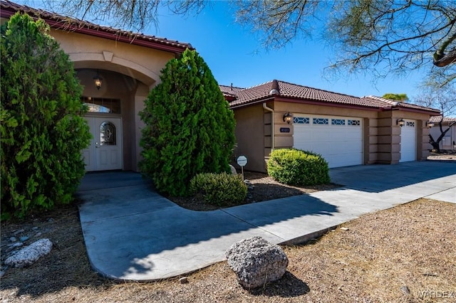 view of front of house featuring a garage, driveway, a tiled roof, and stucco siding