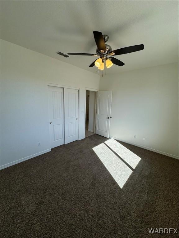 unfurnished bedroom featuring ceiling fan, visible vents, baseboards, a closet, and dark colored carpet