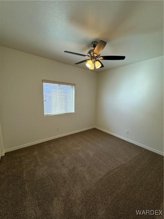 spare room featuring a textured ceiling, ceiling fan, dark carpet, and baseboards