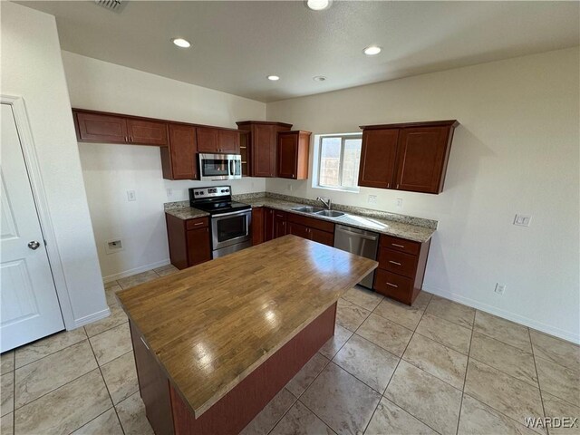 kitchen featuring recessed lighting, appliances with stainless steel finishes, a kitchen island, a sink, and baseboards