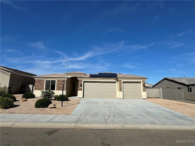 view of front of home with stucco siding, concrete driveway, roof mounted solar panels, fence, and a garage