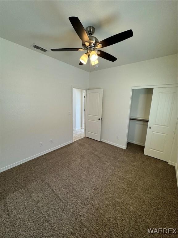 unfurnished bedroom featuring baseboards, visible vents, ceiling fan, dark colored carpet, and a closet