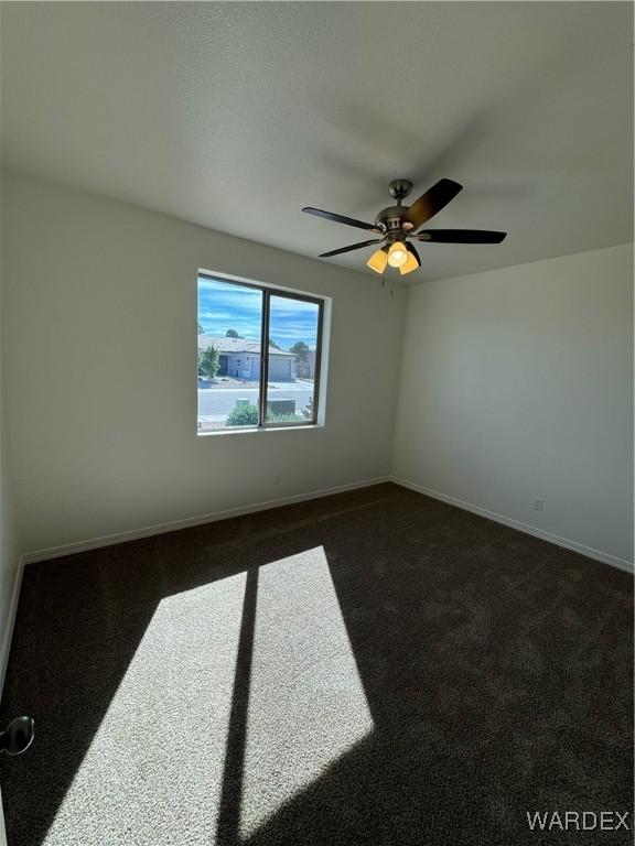 unfurnished room featuring a ceiling fan, dark colored carpet, and baseboards