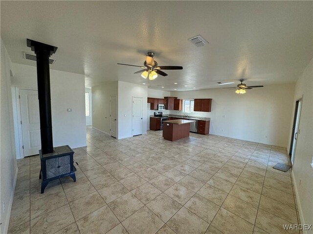 kitchen featuring visible vents, open floor plan, appliances with stainless steel finishes, a center island, and a wood stove