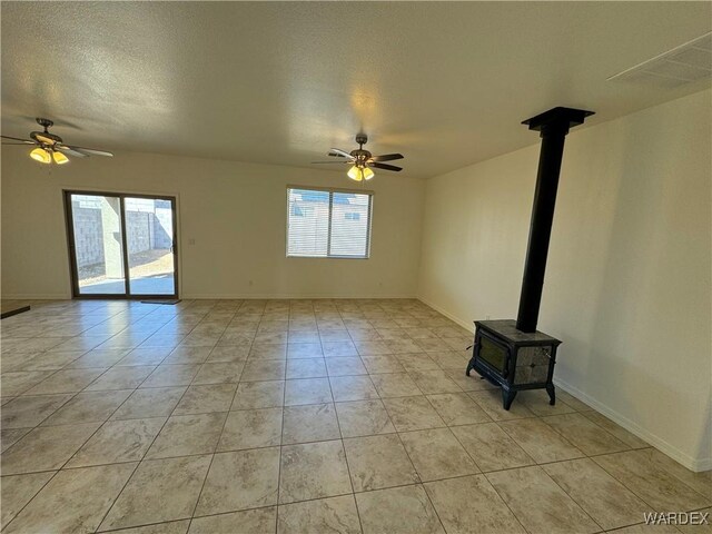 unfurnished living room featuring ceiling fan, a wood stove, and a healthy amount of sunlight