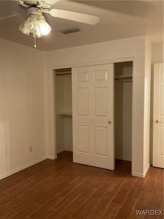 unfurnished bedroom featuring visible vents, baseboards, dark wood-style floors, ceiling fan, and a closet