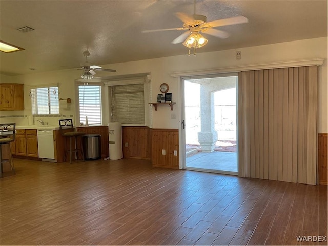 unfurnished living room with a wealth of natural light, wainscoting, dark wood finished floors, and ceiling fan