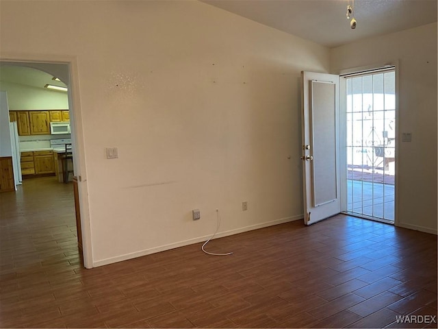 unfurnished room featuring arched walkways, dark wood-style flooring, and baseboards