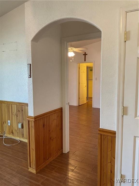 hall with a wainscoted wall, dark wood-type flooring, wood walls, and arched walkways