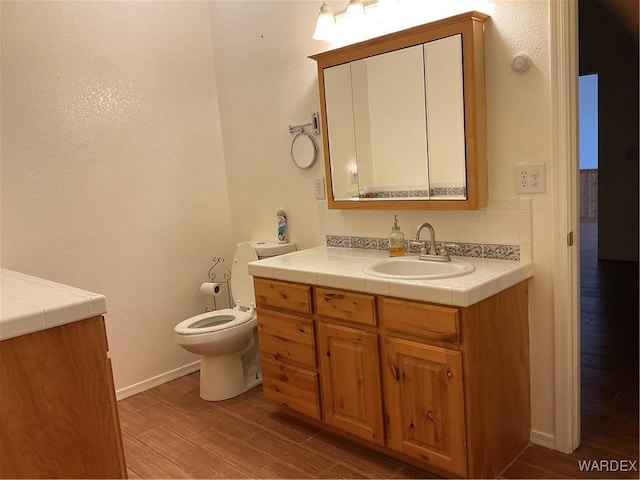 bathroom with baseboards, vanity, toilet, and wood finished floors