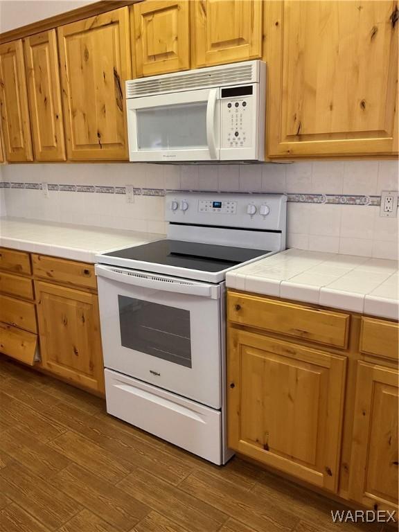 kitchen with white appliances, tasteful backsplash, tile countertops, dark wood-style floors, and brown cabinets