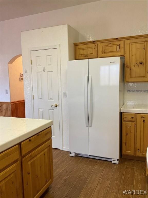 kitchen featuring arched walkways, dark wood-style flooring, brown cabinetry, and freestanding refrigerator