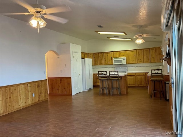 kitchen featuring white appliances, a kitchen island, a breakfast bar area, and arched walkways