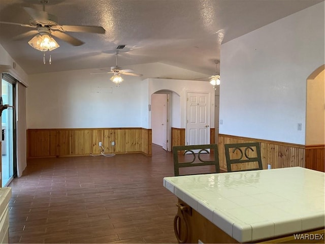 kitchen featuring arched walkways, wainscoting, and tile counters