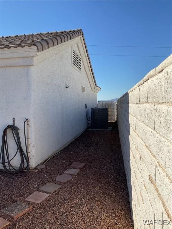 view of home's exterior featuring stucco siding, a tile roof, fence, and central AC unit